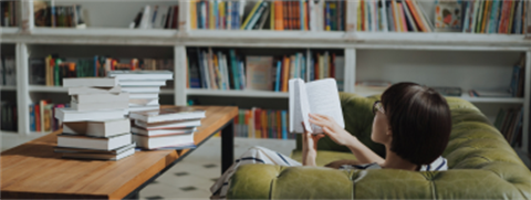 woman reading a book on a green couch in front of a bookcase