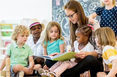 A group of preschool aged children are being read to by an adult woman.